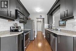 Galley kitchen featuring wood-finish flooring, dark cabinetry, light-toned countertops, and white subway tile backsplash - 