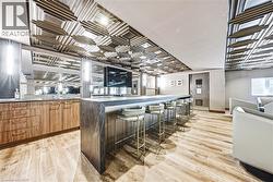 Accent ceiling with geometric paneling and integrated lighting, wood-finish flooring, full-length built-in cabinetry with integrated sink, stone-finish bar with seating, and wall-mounted display - 