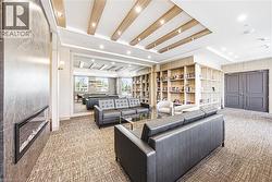 Spacious lounge area featuring a built-in linear electric fireplace, textured carpet flooring, custom built-in shelving, and a coffered ceiling with recessed lighting and wood accents - 