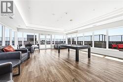 Spacious common area featuring expansive windows, wood-finish flooring, a contemporary ceiling design with recessed lighting, and direct access to an outdoor terrace - 