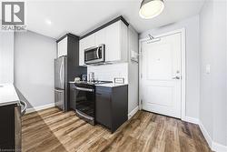Compact kitchen featuring wood-finish flooring, two-tone cabinetry with white upper and dark lower units, stainless steel appliances, white subway tile backsplash, and light countertops - 