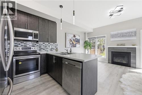 Modern kitchen featuring dark wood-finish cabinetry, stainless steel appliances, a tile backsplash, and light-toned countertops - 37 Delena Avenue S, Hamilton, ON - Indoor Photo Showing Kitchen With Double Sink With Upgraded Kitchen