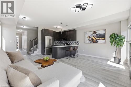 Open-concept living space featuring wood-finish flooring, a contemporary kitchen with dark cabinetry, stainless steel appliances, a breakfast bar, and modern overhead lighting - 37 Delena Avenue S, Hamilton, ON - Indoor