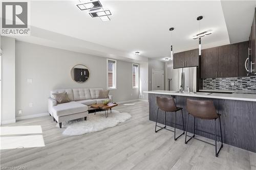 Open-concept living space featuring light wood-finish flooring, a contemporary kitchen island with a white countertop, dark wood-finish cabinetry, stainless steel appliances, and a mosaic tile backspl - 37 Delena Avenue S, Hamilton, ON - Indoor Photo Showing Kitchen With Upgraded Kitchen