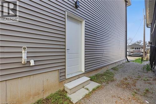 Gray horizontal siding with a white utility door, concrete foundation, and concrete steps - 37 Delena Avenue S, Hamilton, ON - Outdoor