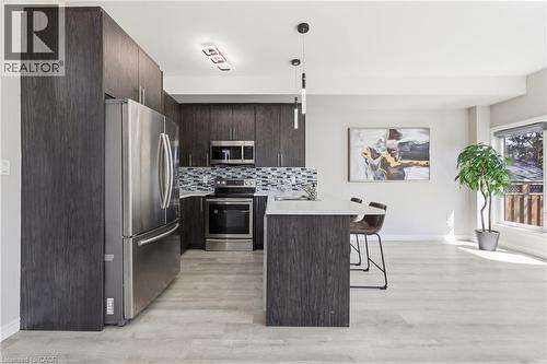 Contemporary kitchen featuring dark wood-finish cabinetry, stainless steel appliances, light-toned wood-finish flooring, a mosaic tile backsplash, and a breakfast bar with pendant lighting - 37 Delena Avenue S, Hamilton, ON - Indoor Photo Showing Kitchen With Upgraded Kitchen