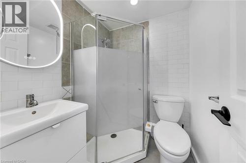 Contemporary bathroom featuring a glass-enclosed shower with frosted paneling, a white vanity with integrated sink, a backlit oval mirror, and white subway tile wainscoting - 501 Ferguson Avenue N, Hamilton, ON - Indoor Photo Showing Bathroom