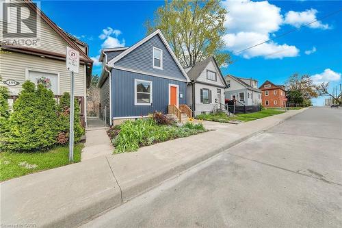 Blue vertical siding exterior featuring a contrasting orange front door, a concrete sidewalk, and a landscaped front yard with varied plantings - 501 Ferguson Avenue N, Hamilton, ON - Outdoor With Facade