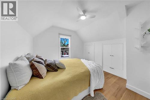 Attic bedroom featuring vaulted ceilings, wood-finish flooring, a built-in ceiling fan with integrated lighting, a window with a roller shade, and built-in storage cabinets with drawer units - 501 Ferguson Avenue N, Hamilton, ON - Indoor Photo Showing Bedroom
