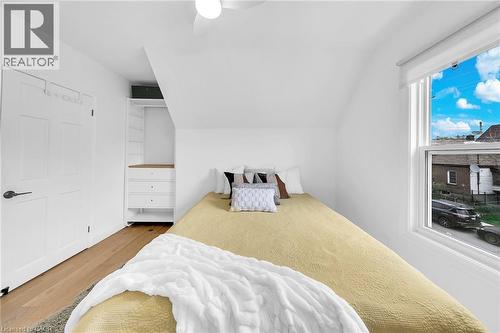 Bright bedroom featuring wood-finish flooring, a built-in closet system with drawers, a white double-panel door, a ceiling fan, and a large window with white trim - 501 Ferguson Avenue N, Hamilton, ON - Indoor Photo Showing Bedroom