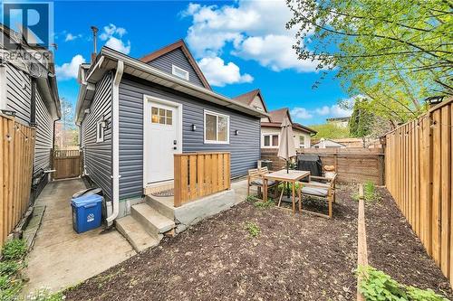Rear exterior featuring dark gray horizontal siding, a white entry door with glass panes, and a concrete patio area with steps - 501 Ferguson Avenue N, Hamilton, ON - Outdoor
