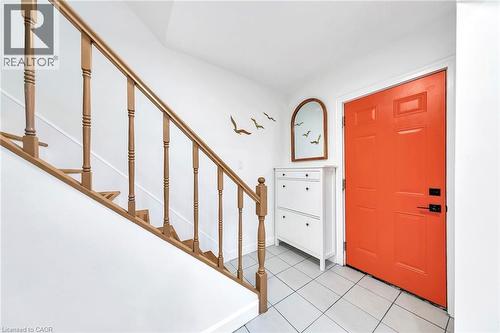 Entryway featuring light-toned square tile flooring, a bright orange paneled door with black hardware, and a wood-toned staircase with turned balusters - 501 Ferguson Avenue N, Hamilton, ON - Indoor Photo Showing Other Room