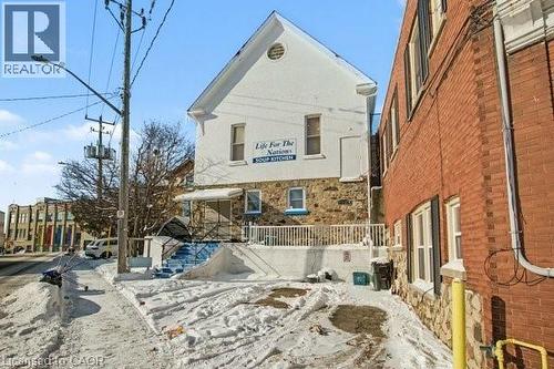 Stone and stucco facade building with a prominent peaked gable, multi-pane windows, blue exterior stairs, and a white railing - 37 Wellington Street, Cambridge, ON 