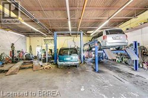 Spacious commercial garage featuring a concrete floor, high ceilings with exposed beams, and fluorescent strip lighting - 9 Meadow Lane S, Hamilton, ON 