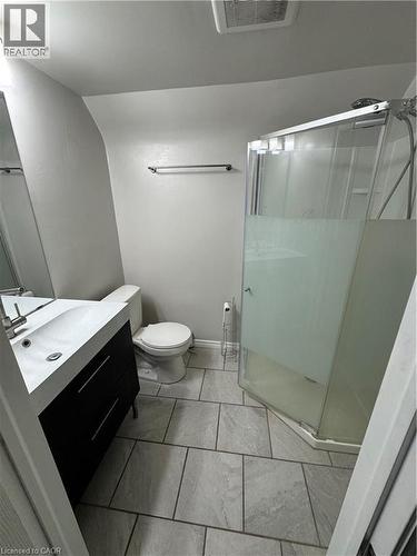 Modern bathroom featuring a corner shower enclosure with frosted glass, a contemporary vanity with dark cabinetry, a rectangular integrated sink, and large format gray tile flooring - 61 Waterloo Drive, Kitchener, ON - Indoor Photo Showing Bathroom