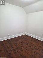 Interior room featuring wood-finish flooring, white baseboards, and a white wall finish with a sloped ceiling detail - 