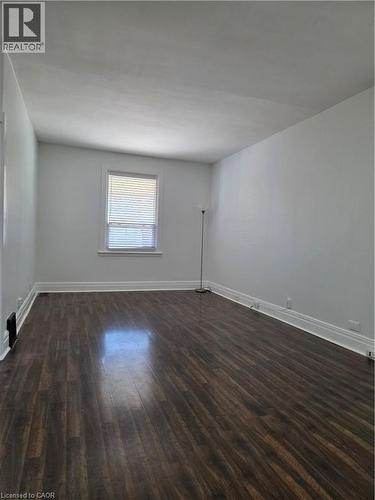 Spacious room featuring dark wood-finish flooring, white baseboards, and a window with horizontal blinds - 125 Cavell Avenue, Hamilton, ON - Indoor Photo Showing Other Room