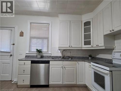White cabinetry with silver hardware, textured gray countertops, subway tile backsplash, stainless steel dishwasher, and wood-finish flooring - 125 Cavell Avenue, Hamilton, ON - Indoor Photo Showing Kitchen With Double Sink