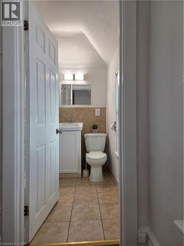 Bathroom featuring a white vanity with integrated sink, a wall-mounted mirror with overhead lighting, a white toilet, and neutral-toned tile flooring - 125 Cavell Avenue, Hamilton, ON - Indoor Photo Showing Bathroom