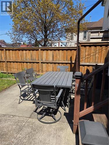 Concrete patio area featuring a wooden privacy fence, mature trees, and a partial view of neighboring structures - 125 Cavell Avenue, Hamilton, ON - Outdoor