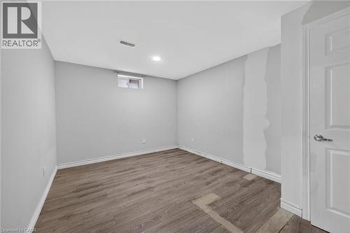 Room featuring wood-finish flooring, a window with roller shades, a flush-mount ceiling light, and a door with a brass-finish knob - 704 Stone Church Road E, Hamilton, ON - Indoor