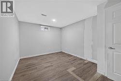 Room featuring wood-finish flooring, a window with roller shades, a flush-mount ceiling light, and a door with a brass-finish knob - 