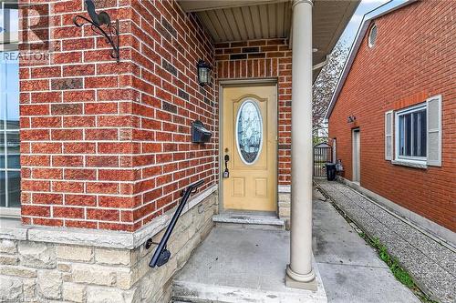 Front entrance featuring a yellow door with oval glass insert, brick facade, stone base, and exterior wall lantern - 704 Stone Church Road E, Hamilton, ON - Outdoor