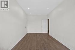 Spacious interior room featuring wood-finish flooring, recessed lighting, neutral wall tones, white trim, and a paneled door - 