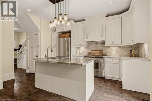 Kitchen featuring white cabinetry, stainless steel appliances, a center island with an integrated sink, stone countertops, and wood-finish flooring - 104 Barnesdale Avenue N, Hamilton, ON - Indoor Photo Showing Kitchen With Upgraded Kitchen