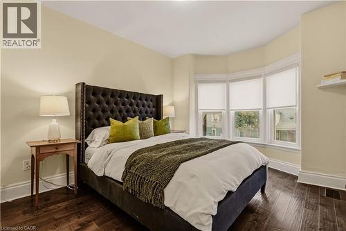 Bay window with three individual windows and roller shades, rich wood-finish flooring, and light-toned walls - 104 Barnesdale Avenue N, Hamilton, ON - Indoor Photo Showing Bedroom