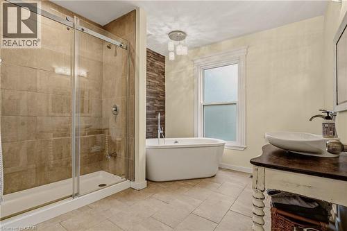 Bathroom featuring a glass-enclosed shower, a freestanding soaking tub, a single window with white trim, a decorative ceiling light fixture, and a vanity with a vessel sink - 104 Barnesdale Avenue N, Hamilton, ON - Indoor Photo Showing Bathroom
