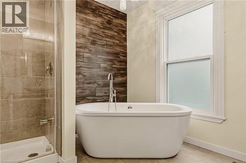 Freestanding soaking tub with a floor-mounted faucet, complemented by a tiled accent wall - 104 Barnesdale Avenue N, Hamilton, ON - Indoor Photo Showing Bathroom