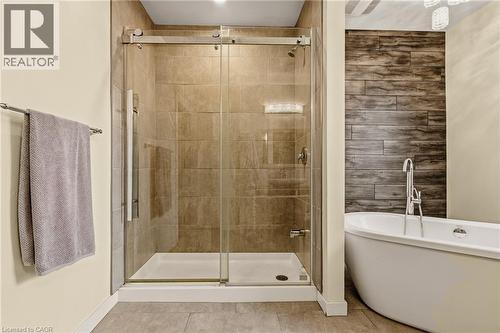 Bathroom featuring a glass-enclosed shower with tile surround, a freestanding soaking tub, wood-finish accent wall, and contemporary light fixture - 104 Barnesdale Avenue N, Hamilton, ON - Indoor Photo Showing Bathroom