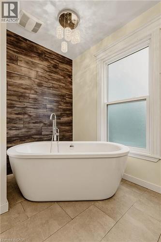 Freestanding soaking tub with a floor-mounted faucet, complemented by a wood-plank accent wall - 104 Barnesdale Avenue N, Hamilton, ON - Indoor Photo Showing Bathroom