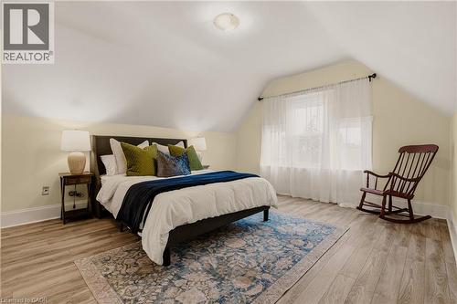 Attic bedroom featuring vaulted ceilings, wood-finish flooring, and a large window with sheer white curtains - 104 Barnesdale Avenue N, Hamilton, ON - Indoor Photo Showing Bedroom