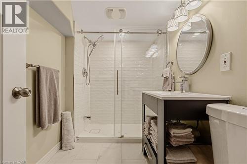 Contemporary bathroom featuring a glass-enclosed shower with white subway tile, a dark wood-finish vanity with an integrated sink, a frameless oval mirror, and a modern chrome light fixture - 104 Barnesdale Avenue N, Hamilton, ON - Indoor Photo Showing Bathroom