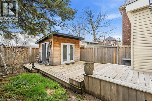 Backyard featuring a spacious wood deck, a modern outbuilding with wood siding and double glass doors, a privacy fence, and a grassy area - 104 Barnesdale Avenue N, Hamilton, ON - Outdoor With Exterior