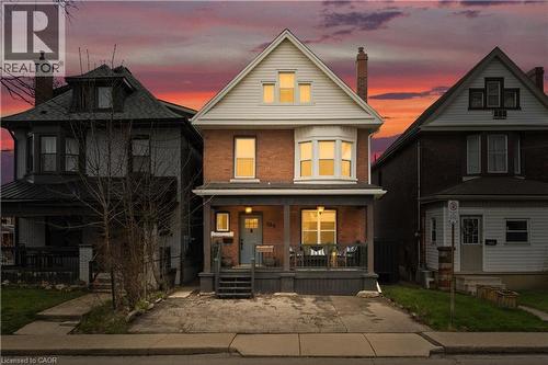 Brick facade residence with a light gray siding gable, featuring a covered front porch, bay window, and gabled dormers - 104 Barnesdale Avenue N, Hamilton, ON - Outdoor With Deck Patio Veranda With Facade