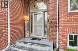 Brick exterior featuring an arched entry door with a storm door, concrete steps, and exterior lighting fixtures - 