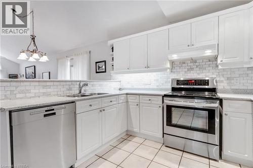 Modern kitchen featuring white cabinetry, subway tile backsplash, stainless steel appliances, a double basin sink, and tile flooring - 422 Powerline Road Unit# 10, Brantford, ON - Indoor Photo Showing Kitchen