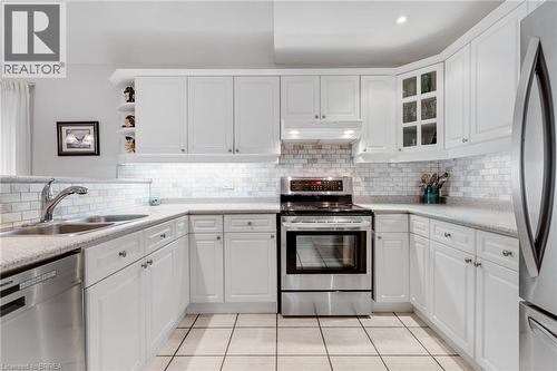 U-shaped kitchen featuring white cabinetry, light-toned countertops, subway tile backsplash, stainless steel appliances, and square floor tiles - 422 Powerline Road Unit# 10, Brantford, ON - Indoor Photo Showing Kitchen With Stainless Steel Kitchen With Double Sink