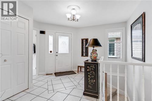 Entryway featuring white square tile flooring with a geometric inlay, a white front door with frosted glass inserts, and an overhead three-light fixture - 422 Powerline Road Unit# 10, Brantford, ON - Indoor Photo Showing Other Room