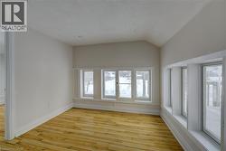 Room featuring wood-finish flooring, multiple windows providing natural illumination, and a vaulted ceiling detail - 