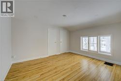 Spacious room featuring wood-finish flooring, white walls, and a triple-pane window unit - 