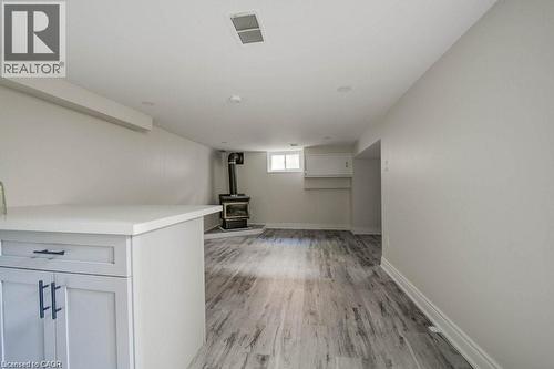Spacious room featuring wood-finish flooring, a built-in white countertop with light gray cabinetry, and a black wood-burning stove with a protective hearth - 33 Sixth Avenue, Kitchener, ON - Indoor Photo Showing Other Room