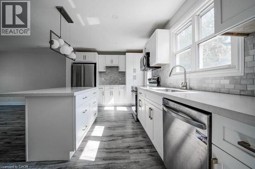 Sleek kitchen featuring white shaker cabinetry, an expansive island with storage, stainless steel appliances, wood-finish flooring, and a subway tile backsplash - 33 Sixth Avenue, Kitchener, ON - Indoor Photo Showing Kitchen With Upgraded Kitchen