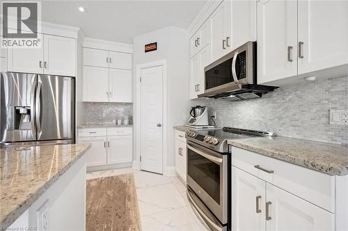 White kitchen featuring stainless steel appliances, granite countertops, white shaker cabinetry, and a mosaic tile backsplash - 72 Elmbank Trail, Kitchener, ON - Indoor Photo Showing Kitchen With Upgraded Kitchen
