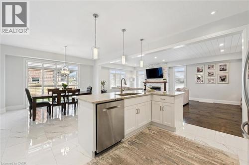 Open-concept living space with a kitchen island featuring a stainless steel dishwasher, white shaker cabinetry, and granite countertops - 72 Elmbank Trail, Kitchener, ON - Indoor