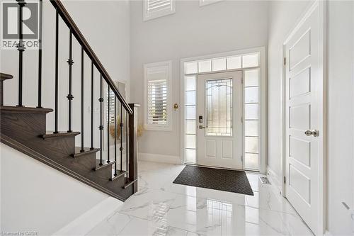 Bright entryway featuring white marble-look tile flooring, a white paneled entry door with frosted sidelights and transom windows, and a dark wood staircase with black iron balusters - 72 Elmbank Trail, Kitchener, ON - Indoor Photo Showing Other Room