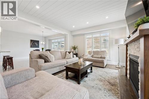 Spacious living area featuring a wood-finish flooring, a stone-faced fireplace with a wood mantle, white plantation shutters, and a slatted ceiling with recessed lighting - 72 Elmbank Trail, Kitchener, ON - Indoor Photo Showing Living Room With Fireplace